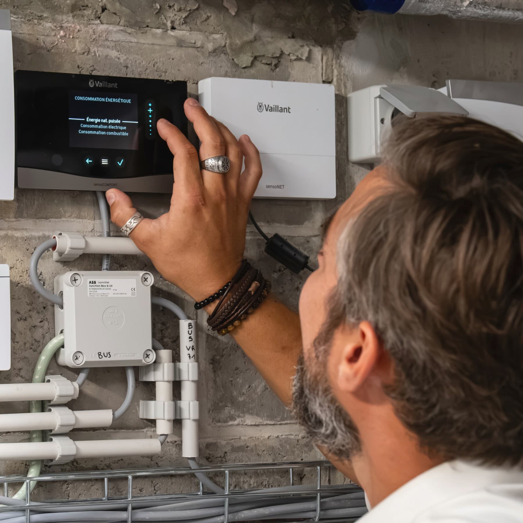 Man past instellingen aan op thermostaat, naast de thermostaat hangt een internetmodule
