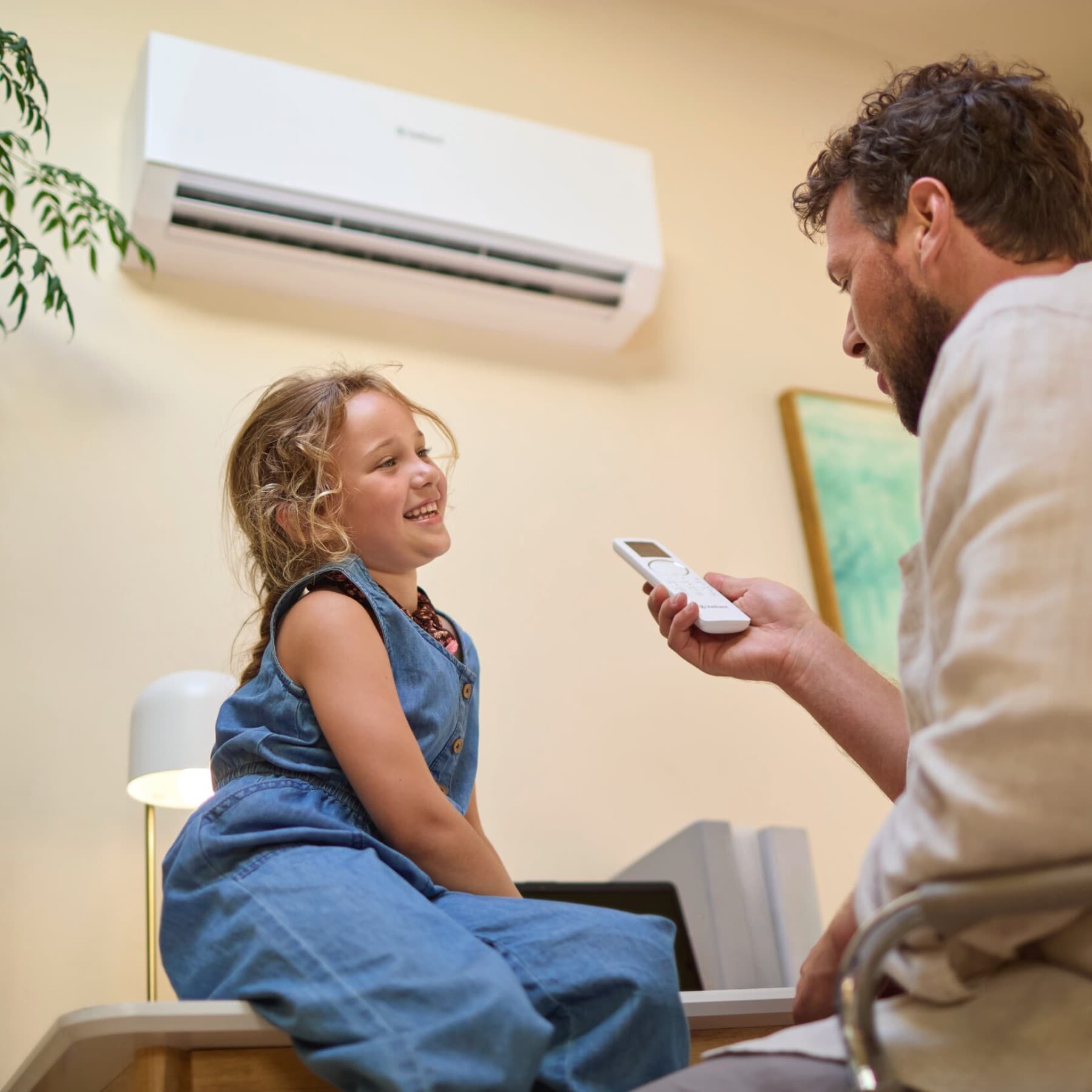 Kind zit op een bureau en man houdt de afstandsbediening vast van een airco