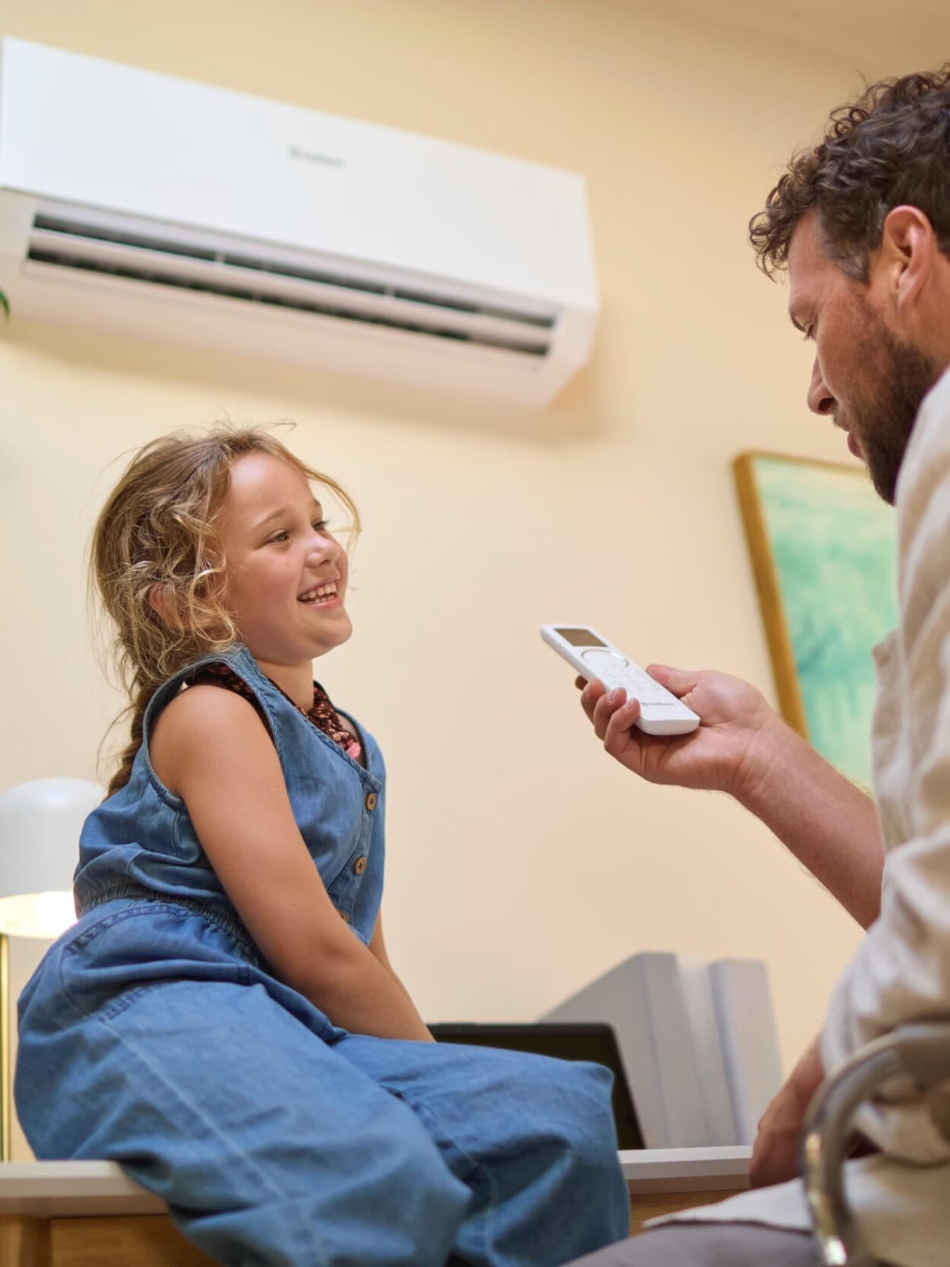 Kind zit op een tafel, man heeft de bediening van zijn airco vast