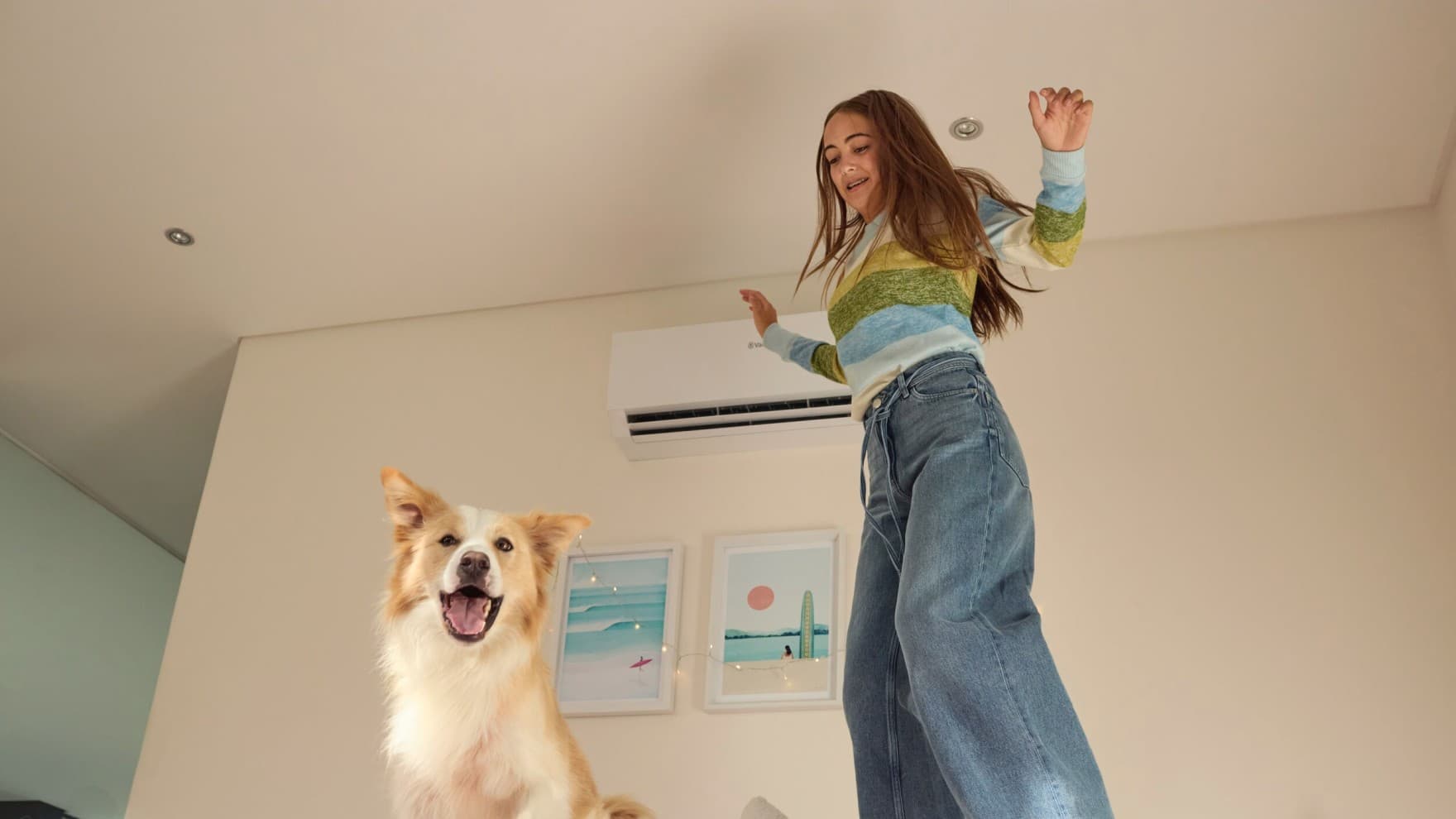 Meisje springt met haar hond op het bed, op de achtergrond zie je de binnenunit van een airco