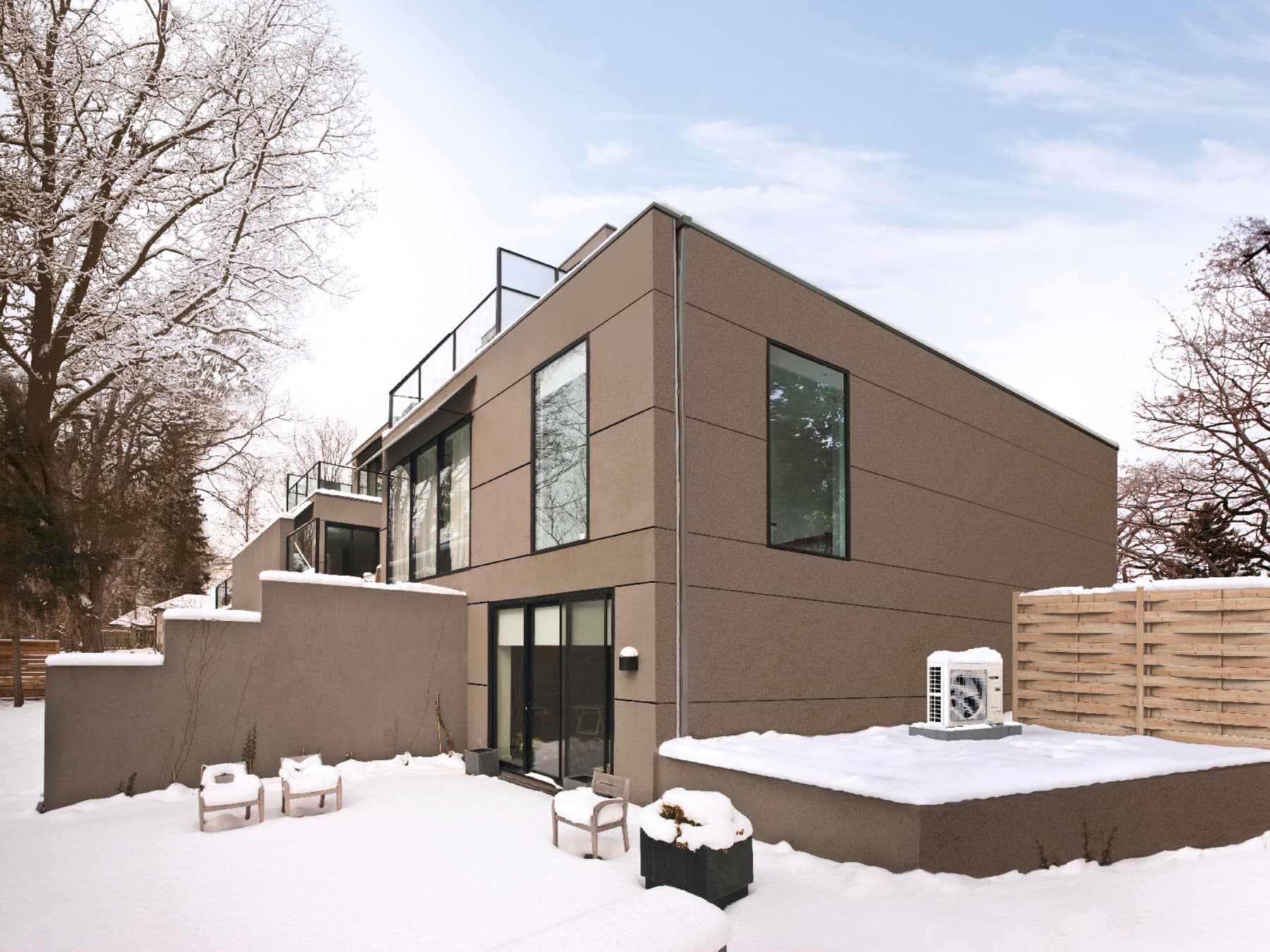 Woning met een grijsbruine gevel en zwarte raamkozijnen, het is gesneeuwd en er staan stoelen in de tuin en een airco buitenunit op een verhoog.