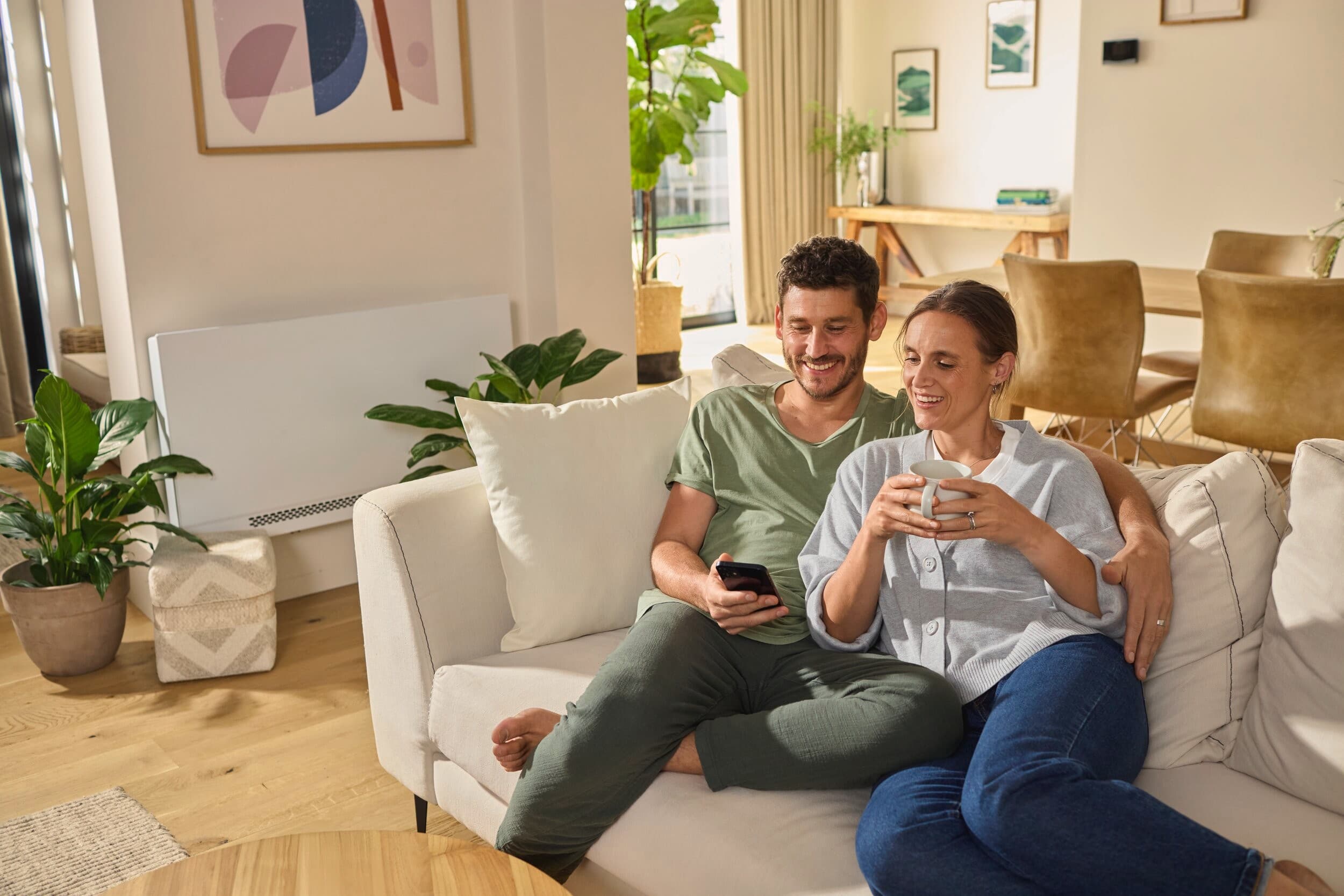 Een stel dat op de bank zit te ontspannen, met op de achtergrond een aroVAIR plus-ventilatorconvector