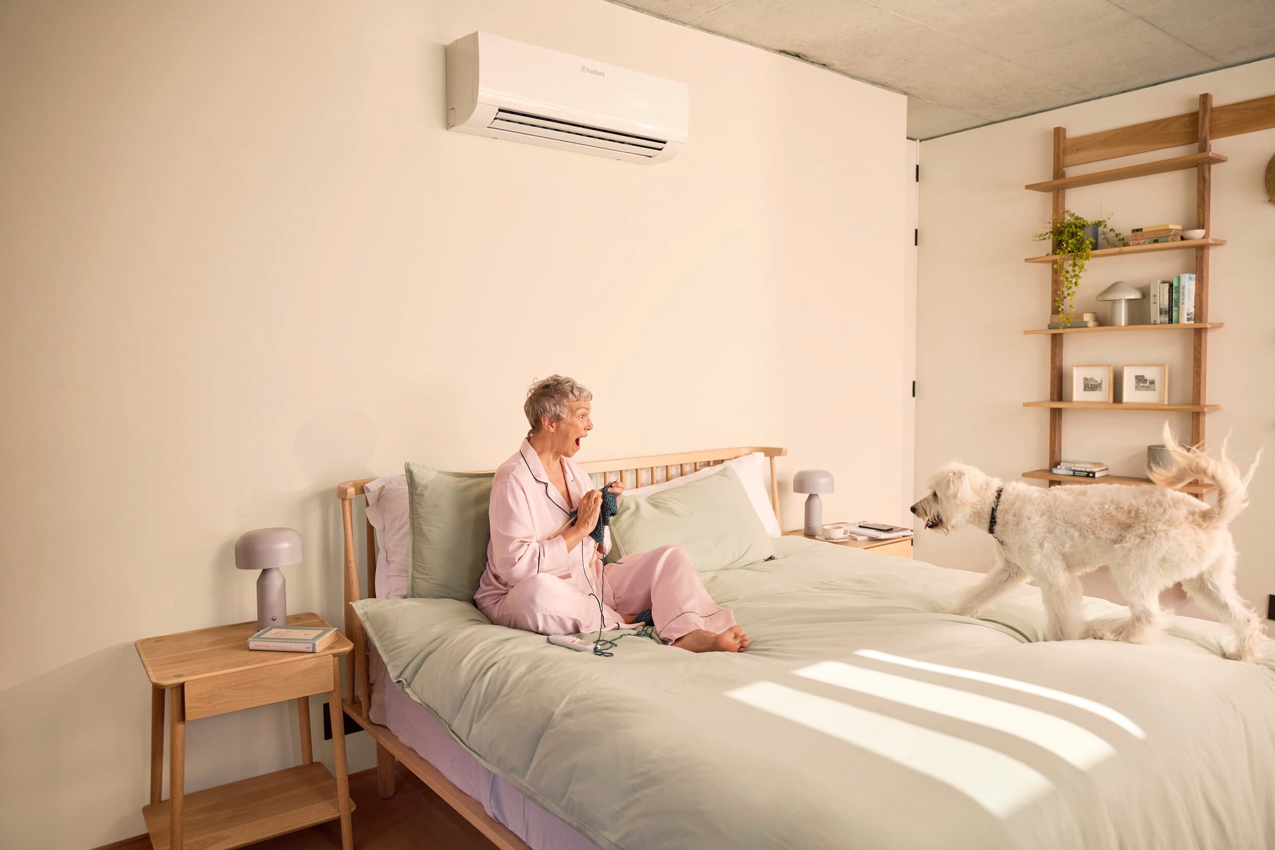 Een vrouw zit in haar bed terwijl haar hond naar haar toe komt