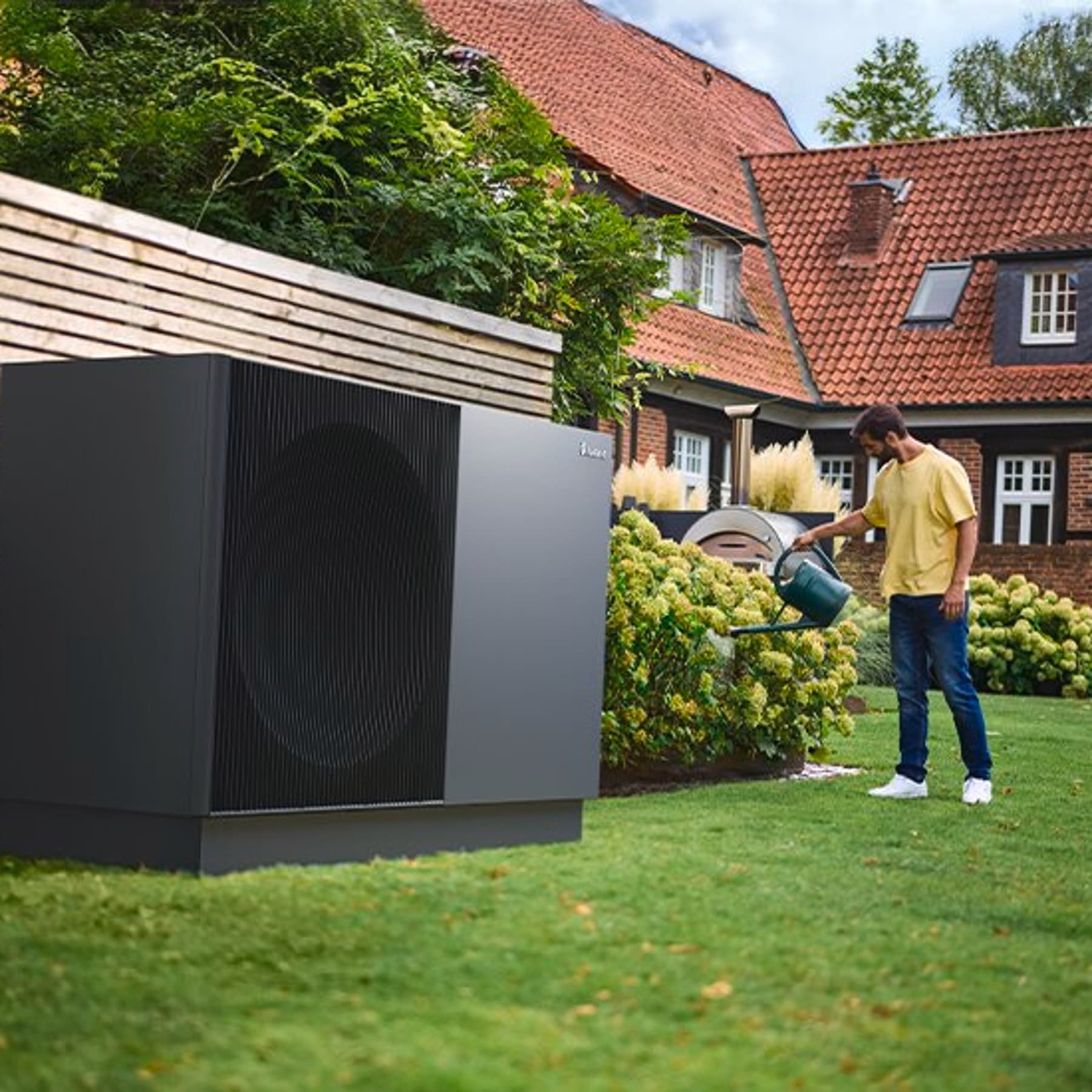 aroTHERM perform warmtepomp in een tuin terwijl een man water geeft aan bloemen