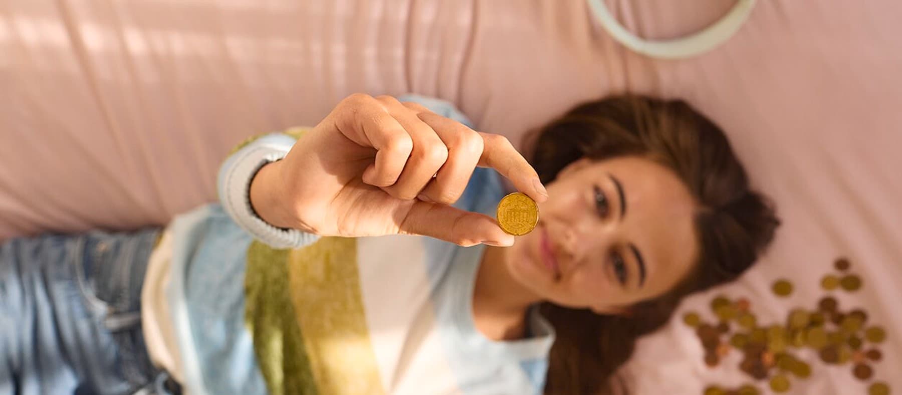 Une femme est allongée sur son lit et tient une pièce de monnaie en l'air
