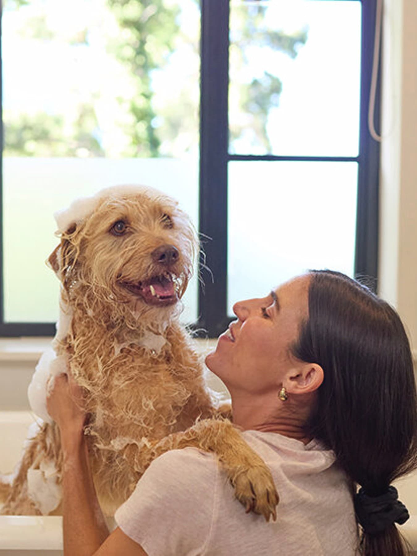 Vrouw wast beige hond in een bad, de hond hijgt