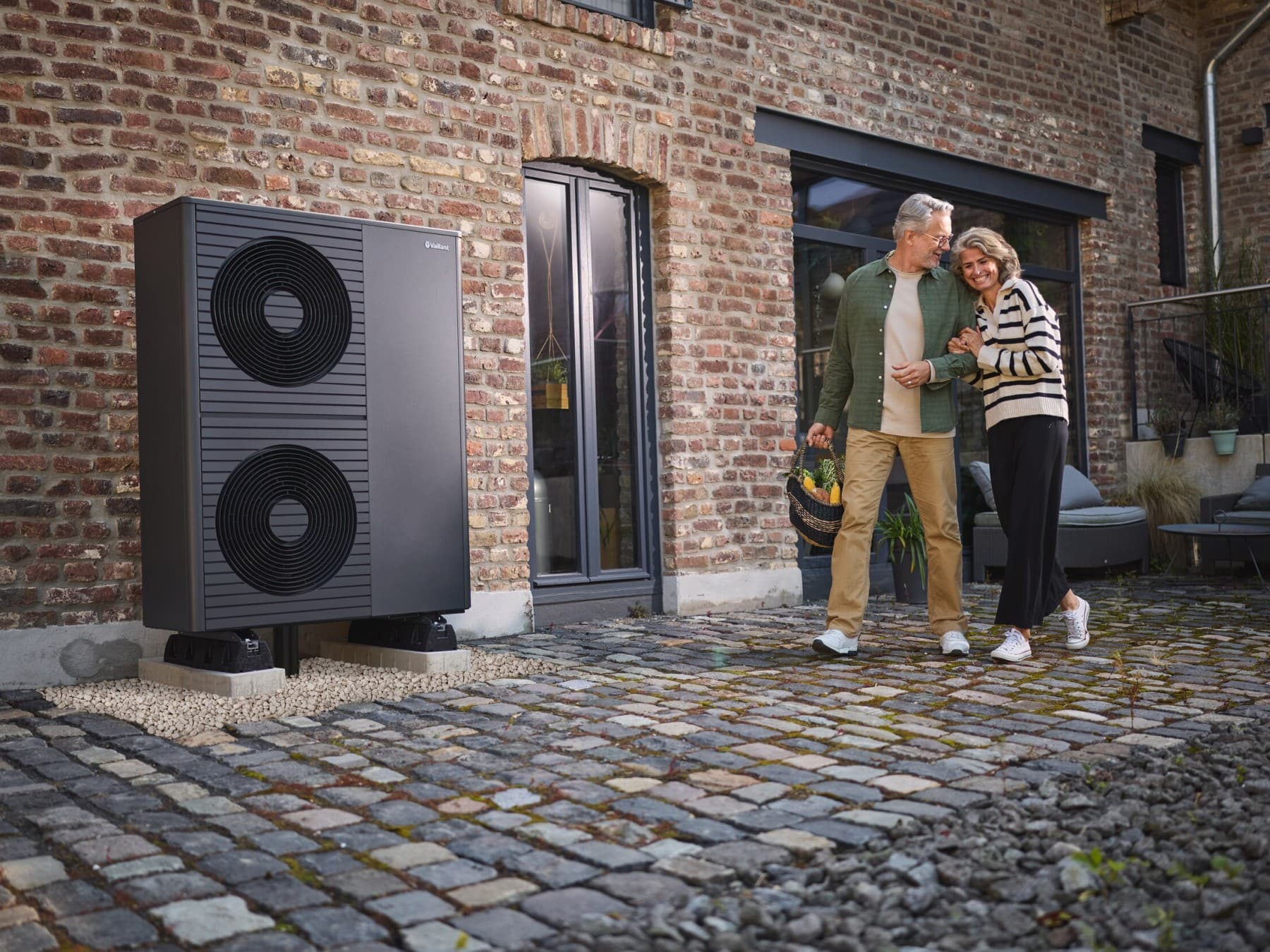 Stel loopt buiten het huis, warmtepomp bevindt zich aan de muur.