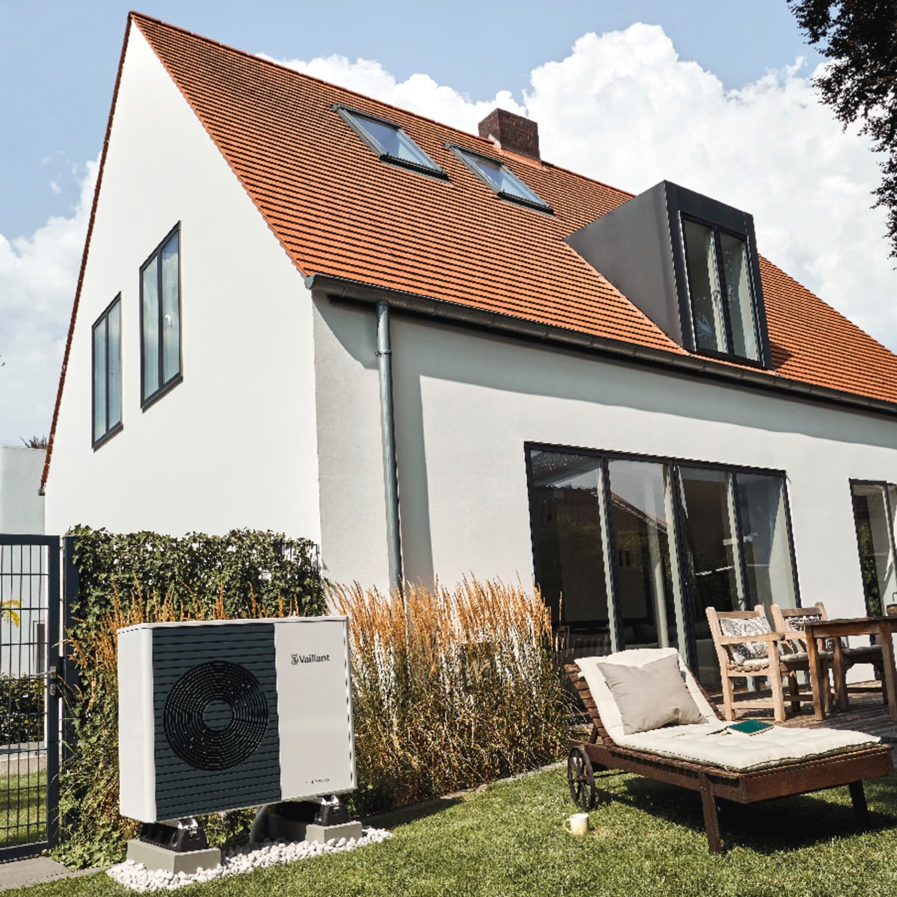 Woning van witte crepi met zwarte raamkozijnen. In de tuin staan ligsteoelen en staat de witte buitenunit van een warmtepomp