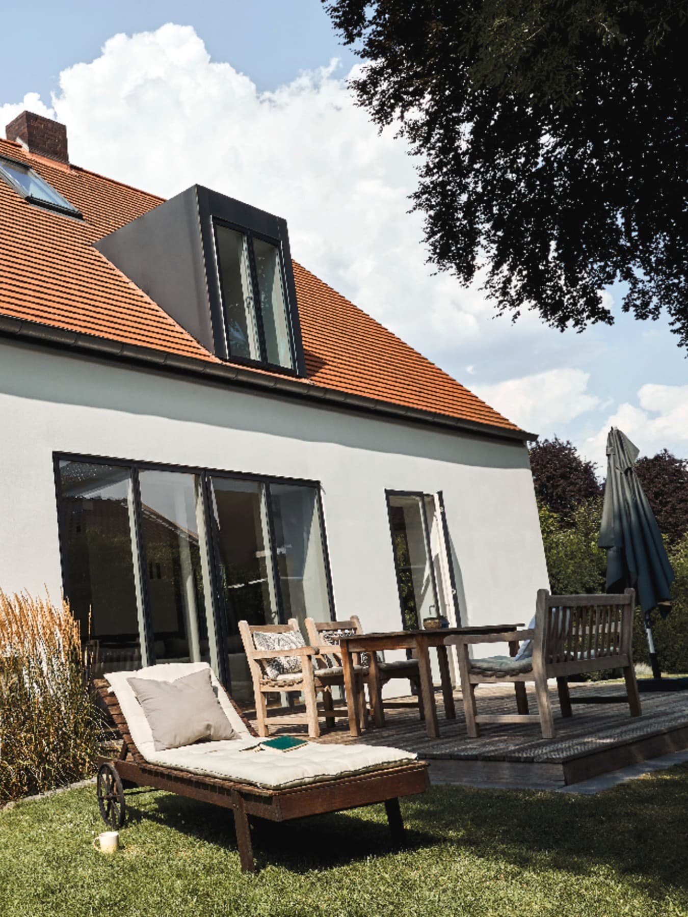 Woning van witte crepi met zwarte raamkozijnen. In de tuin staan ligsteoelen en staat de witte buitenunit van een warmtepomp
