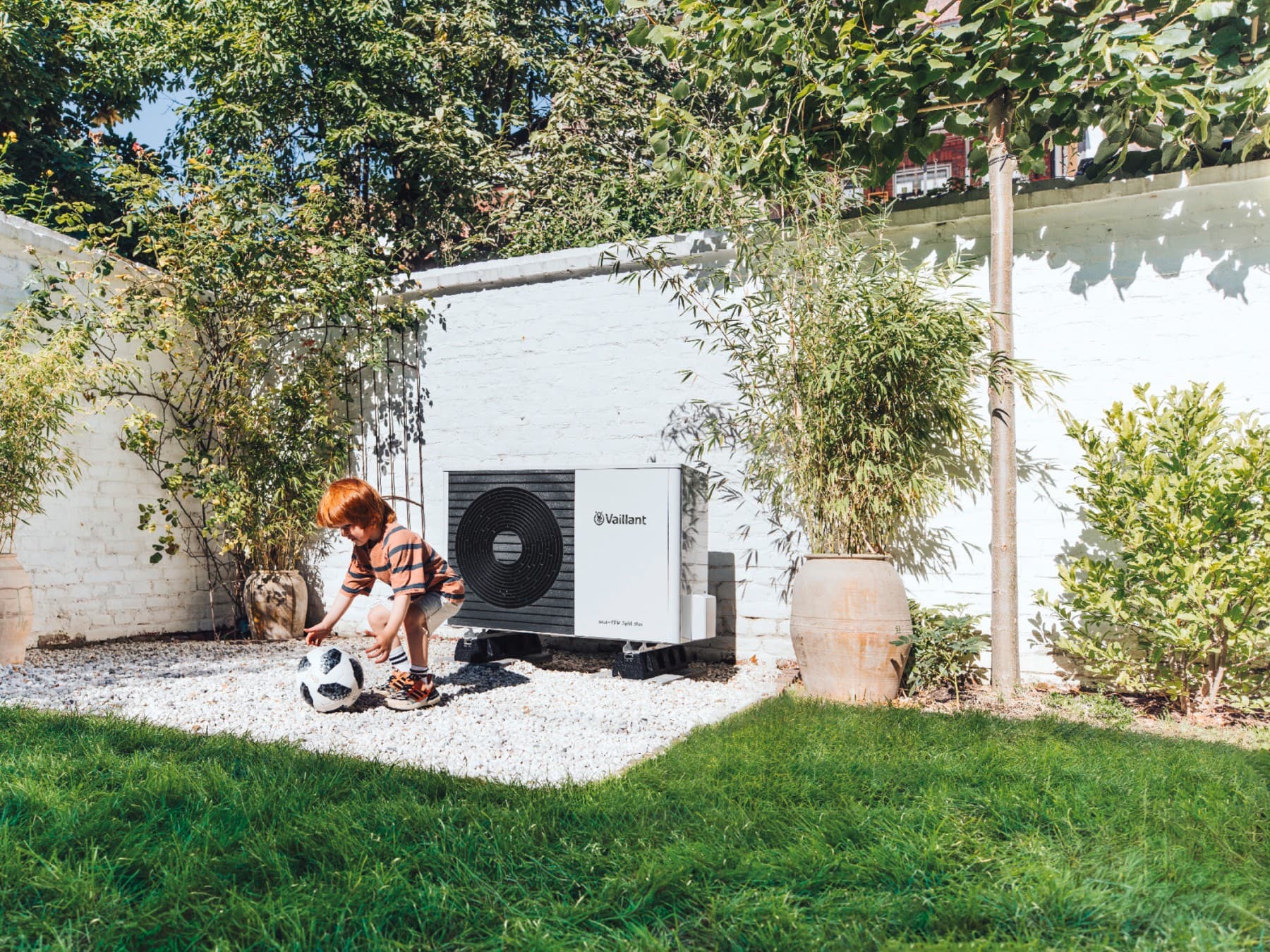 kind dat met een bal speelt voor een warmtepomp in de tuin