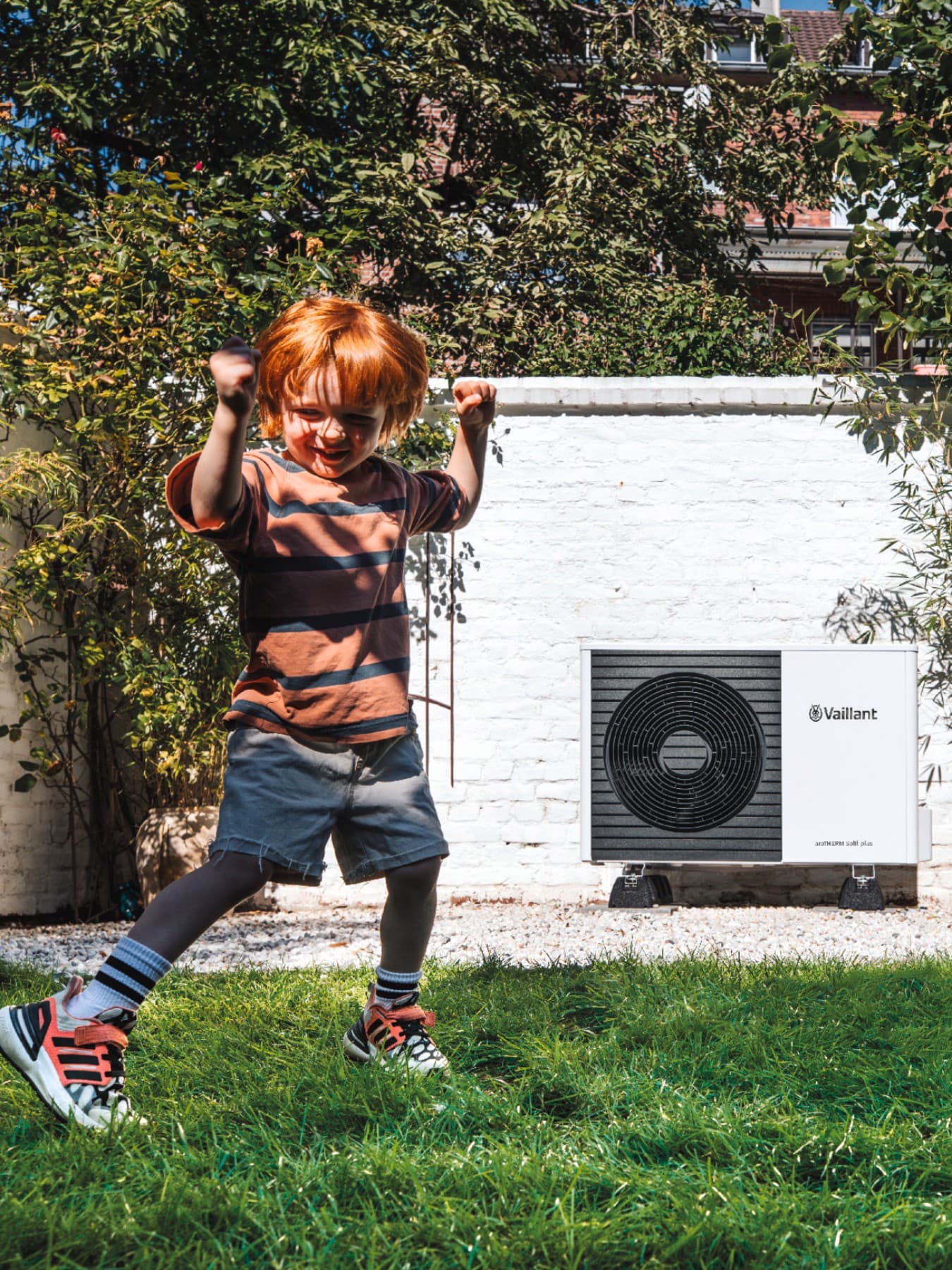 Kind speelt met vader in de tuin met warmtepomp op de achtergrond