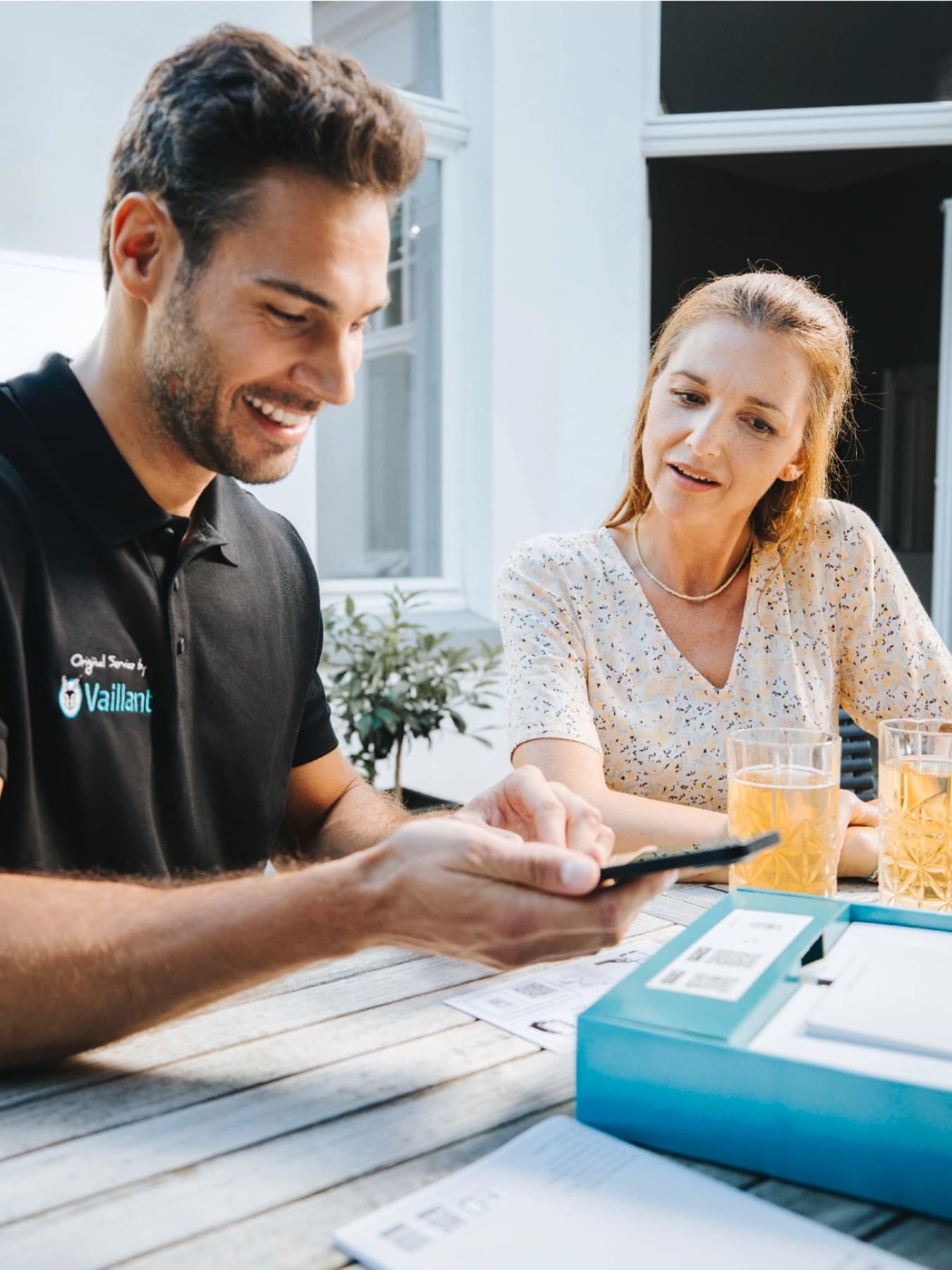 Een Vaillant-installateur met een smartphone in de hand en een klant die naast hem zit