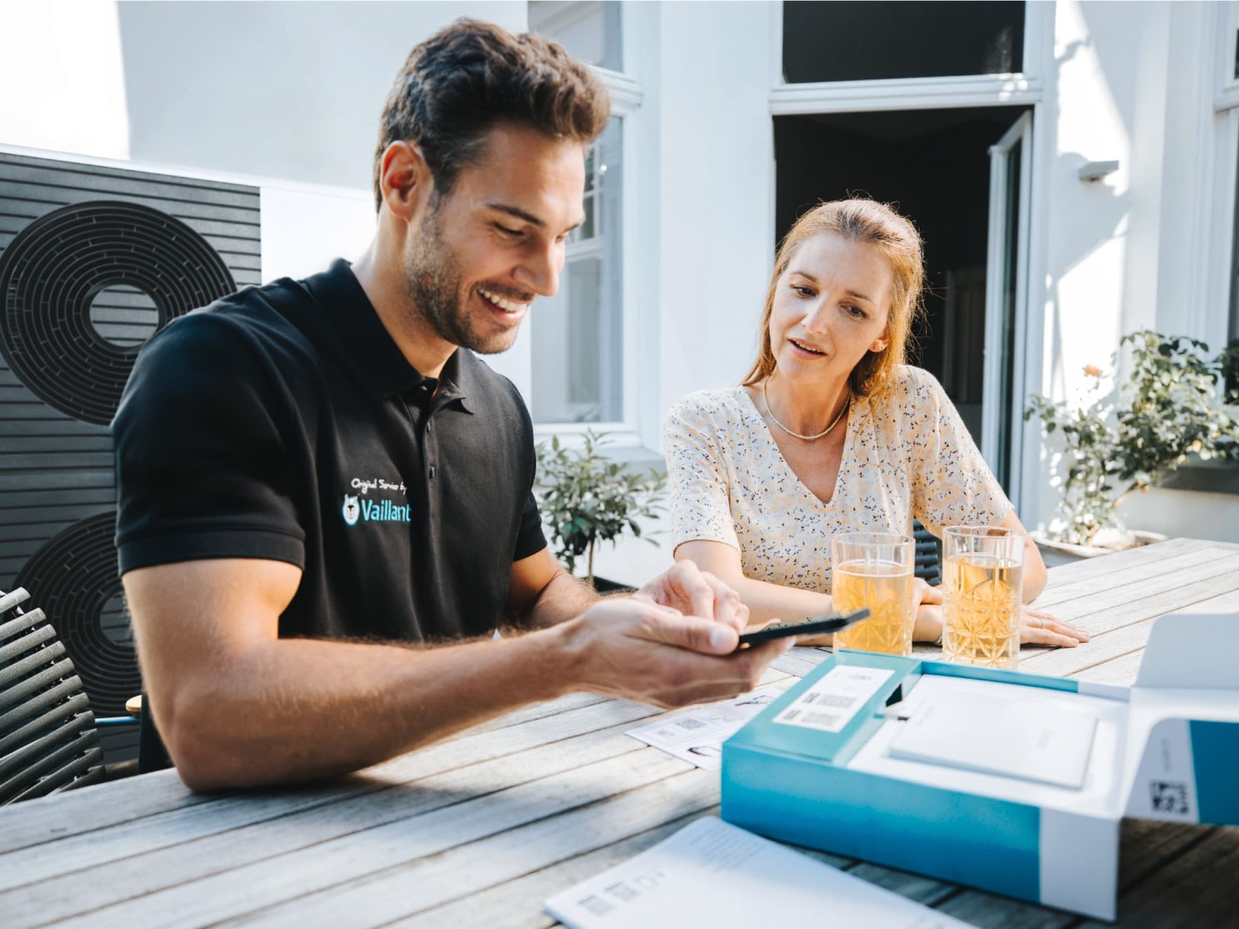 Een Vaillant-installateur met een smartphone in de hand en een klant die naast hem zit