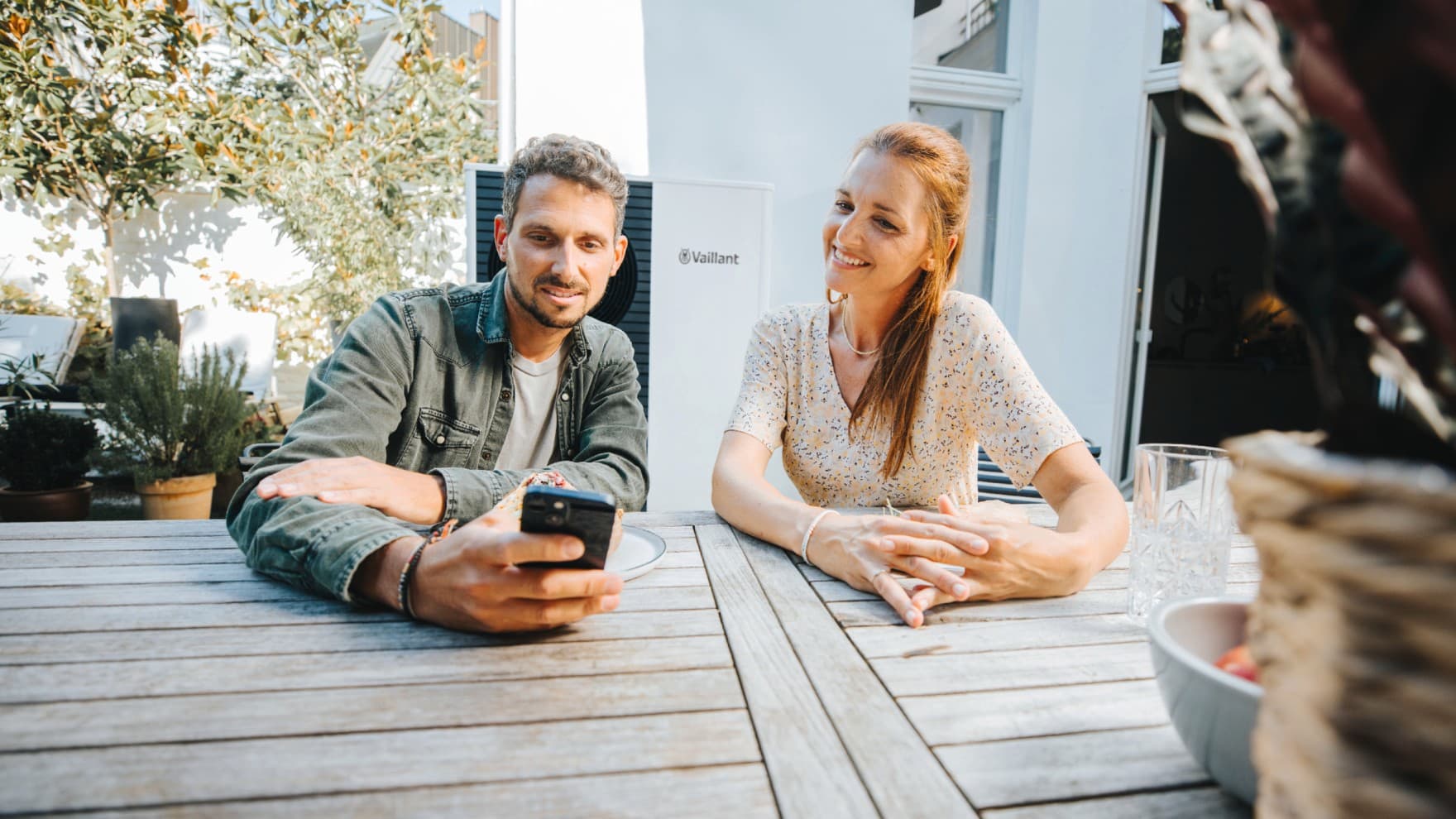 Een stel zit aan een tafel in de tuin en kijkt naar hun smartphone.