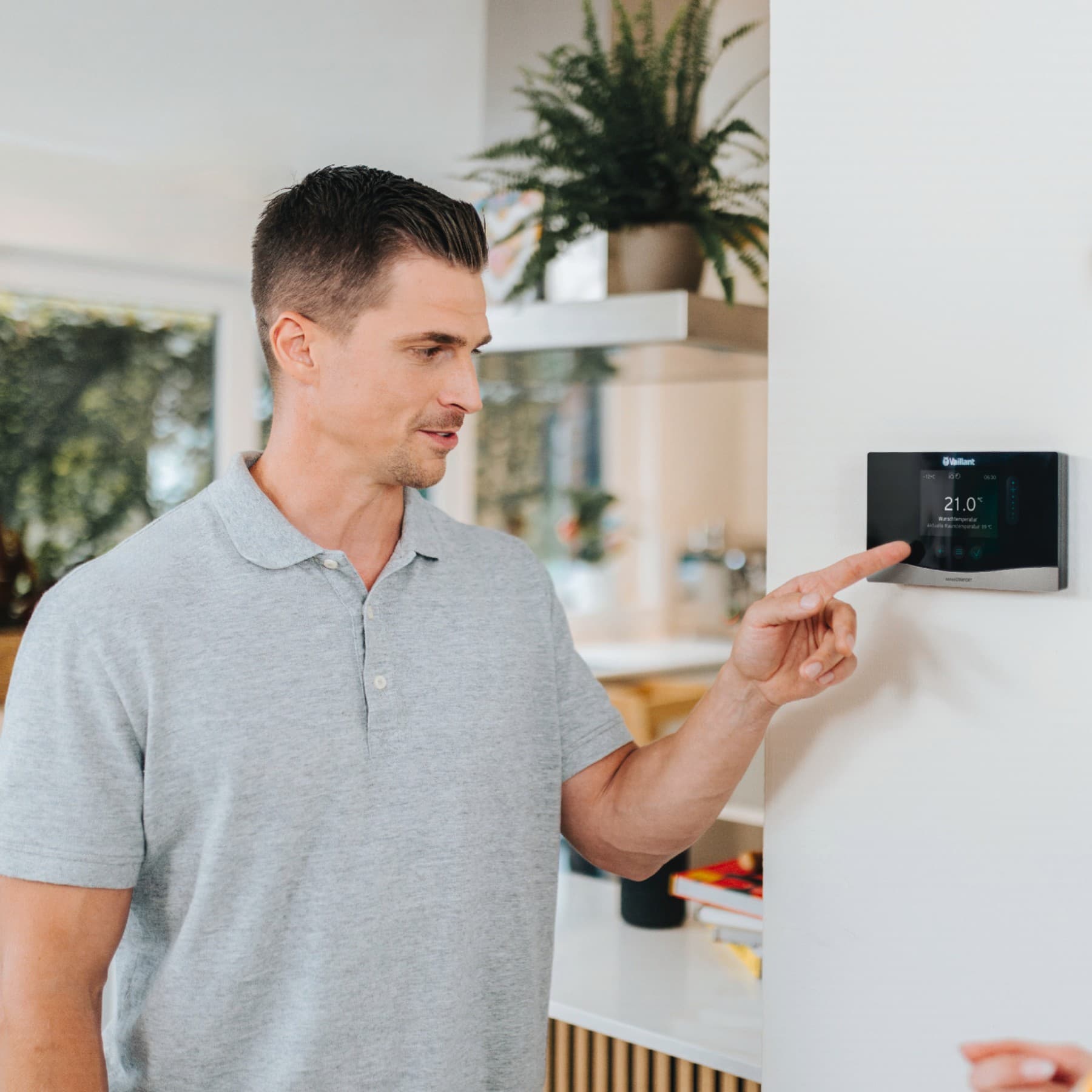 Man wijst naar thermostaat die aan de muur hangt terwijl een vrouw naar het scherm kijkt