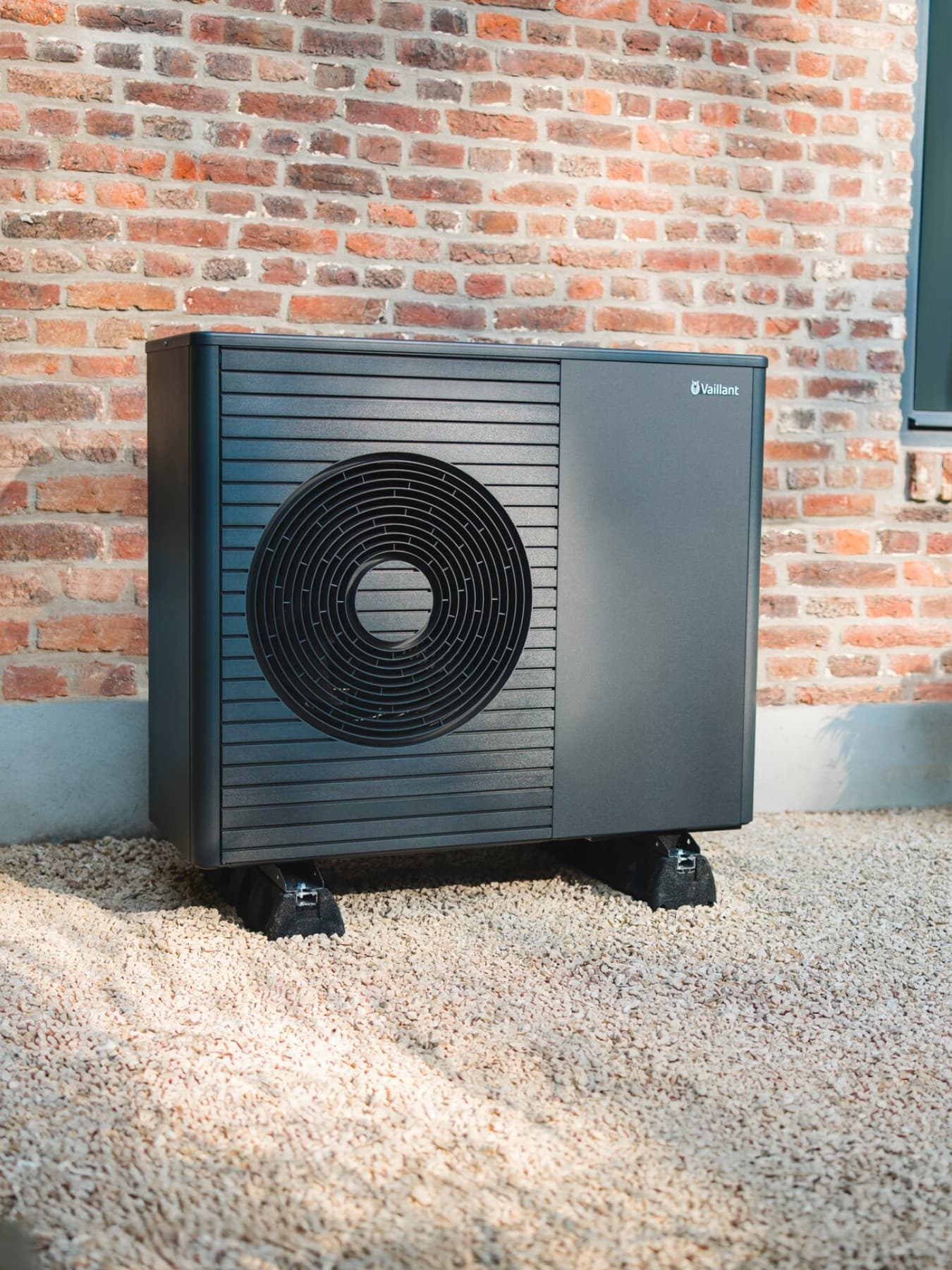 Een warmtepomp staat voor een nieuw gebouw, met een goed onderhouden gazon en een pad op de voorgrond.