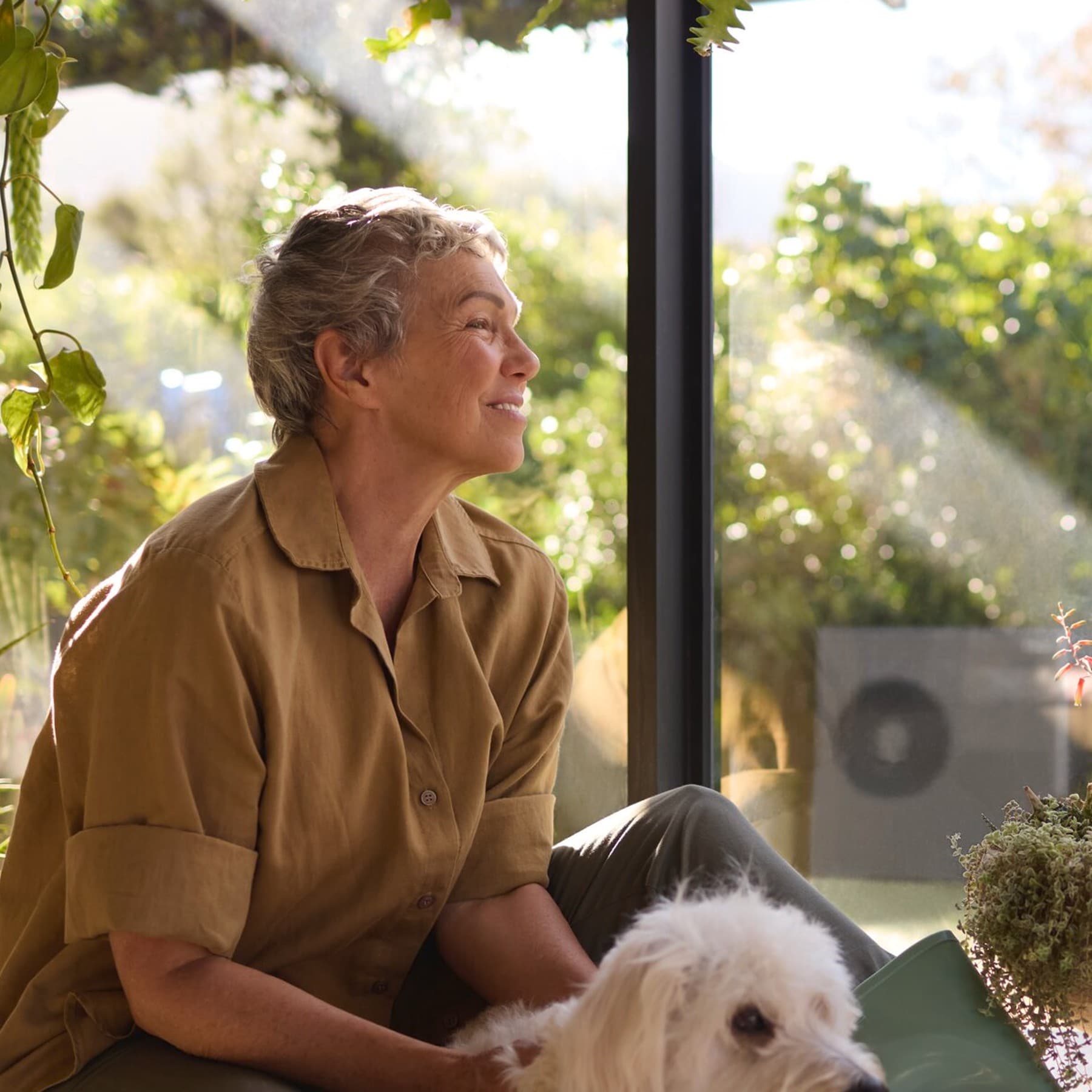 Een vrouw zit met haar hond bij het raam