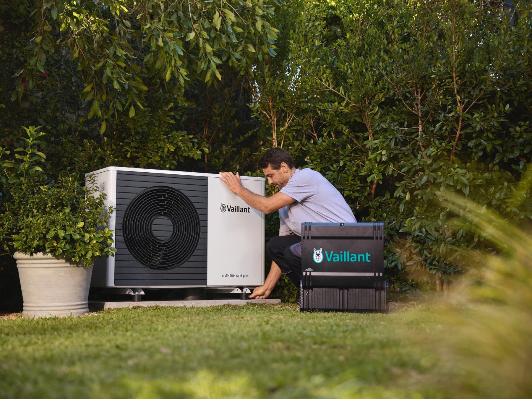 Een technieker die aan een warmtepomp in de tuin werkt | Vaillant