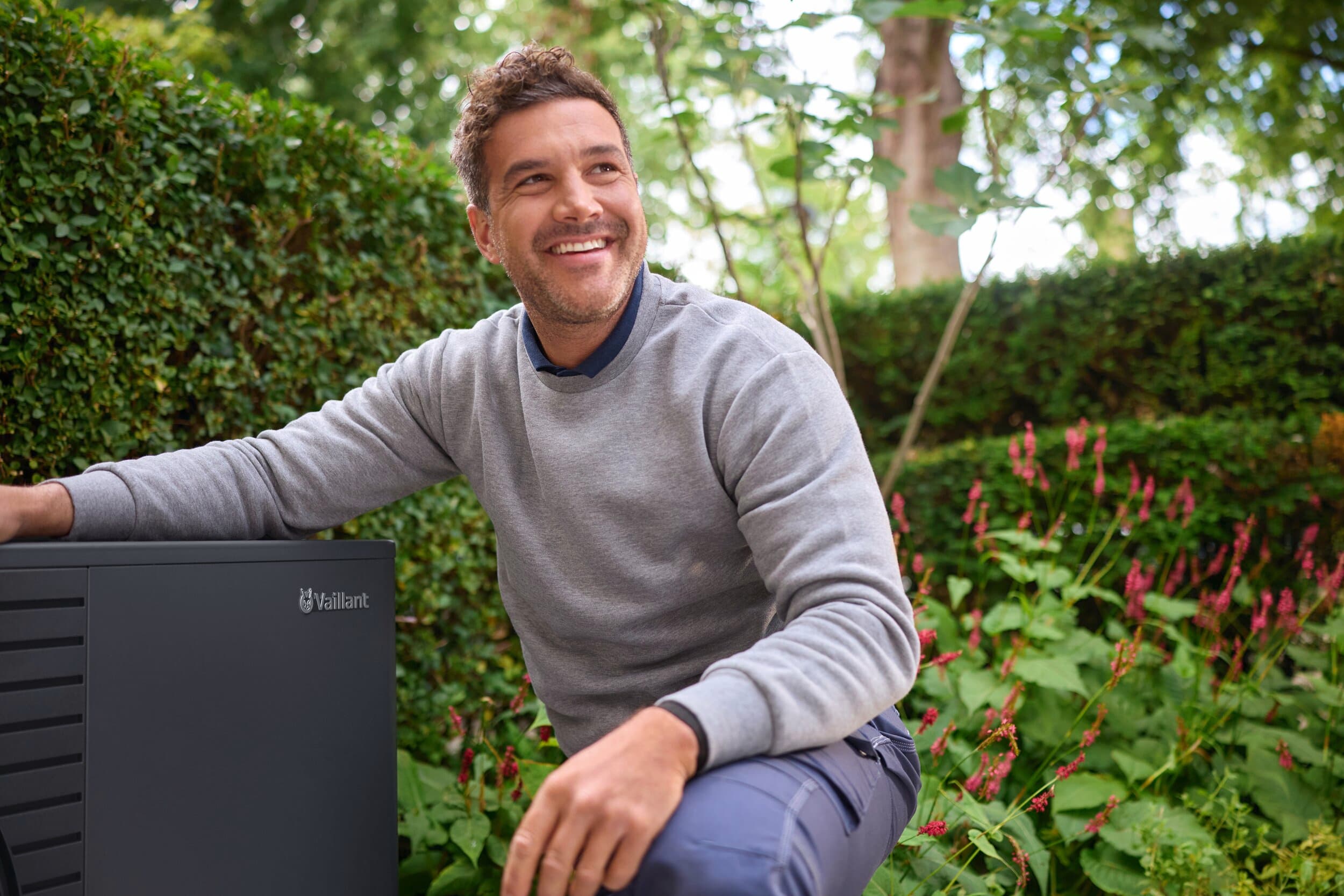Man die naast een aroTHERM pro in de tuin knielt