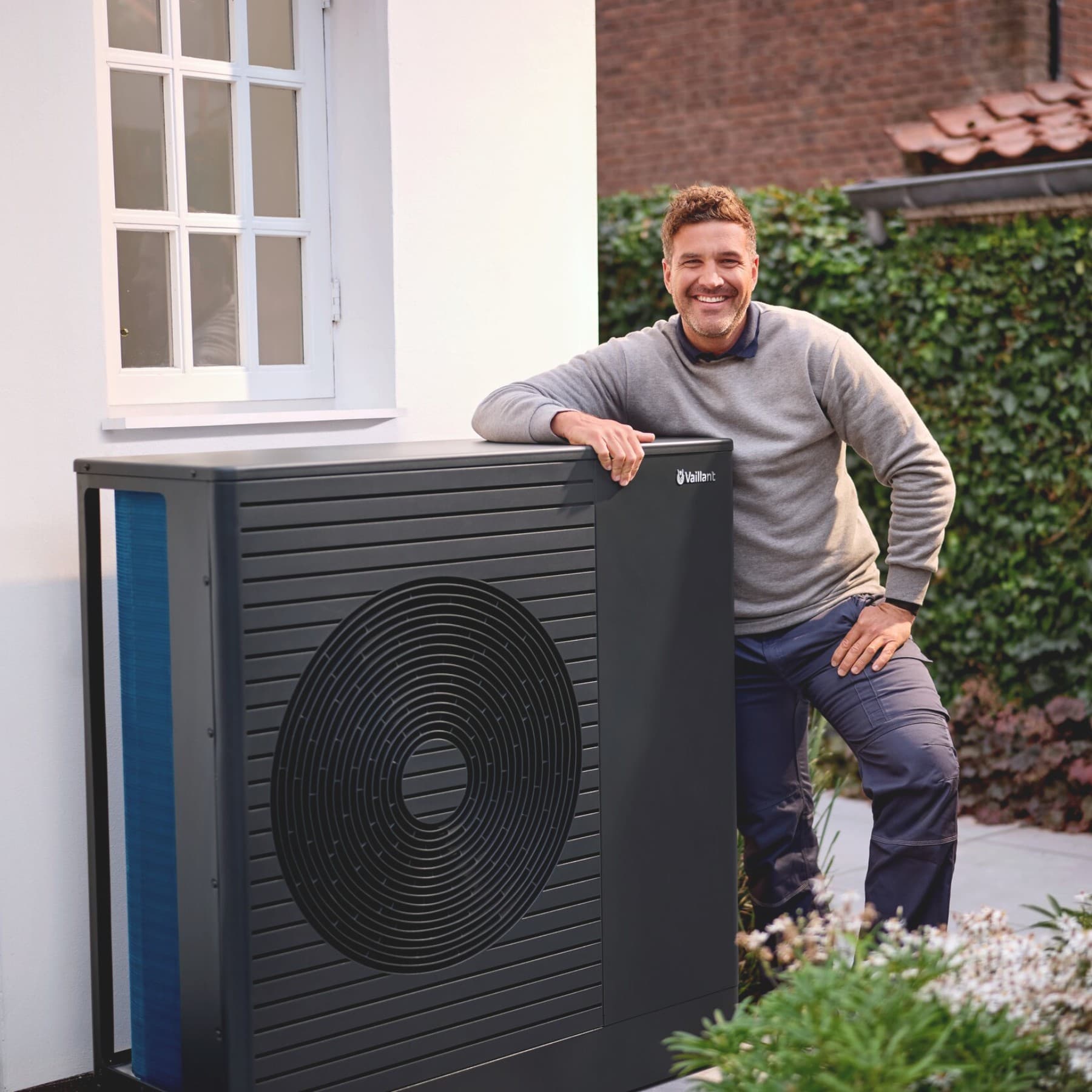 Installateur leunt op een buitenunit van een warmtepomp naast een woning