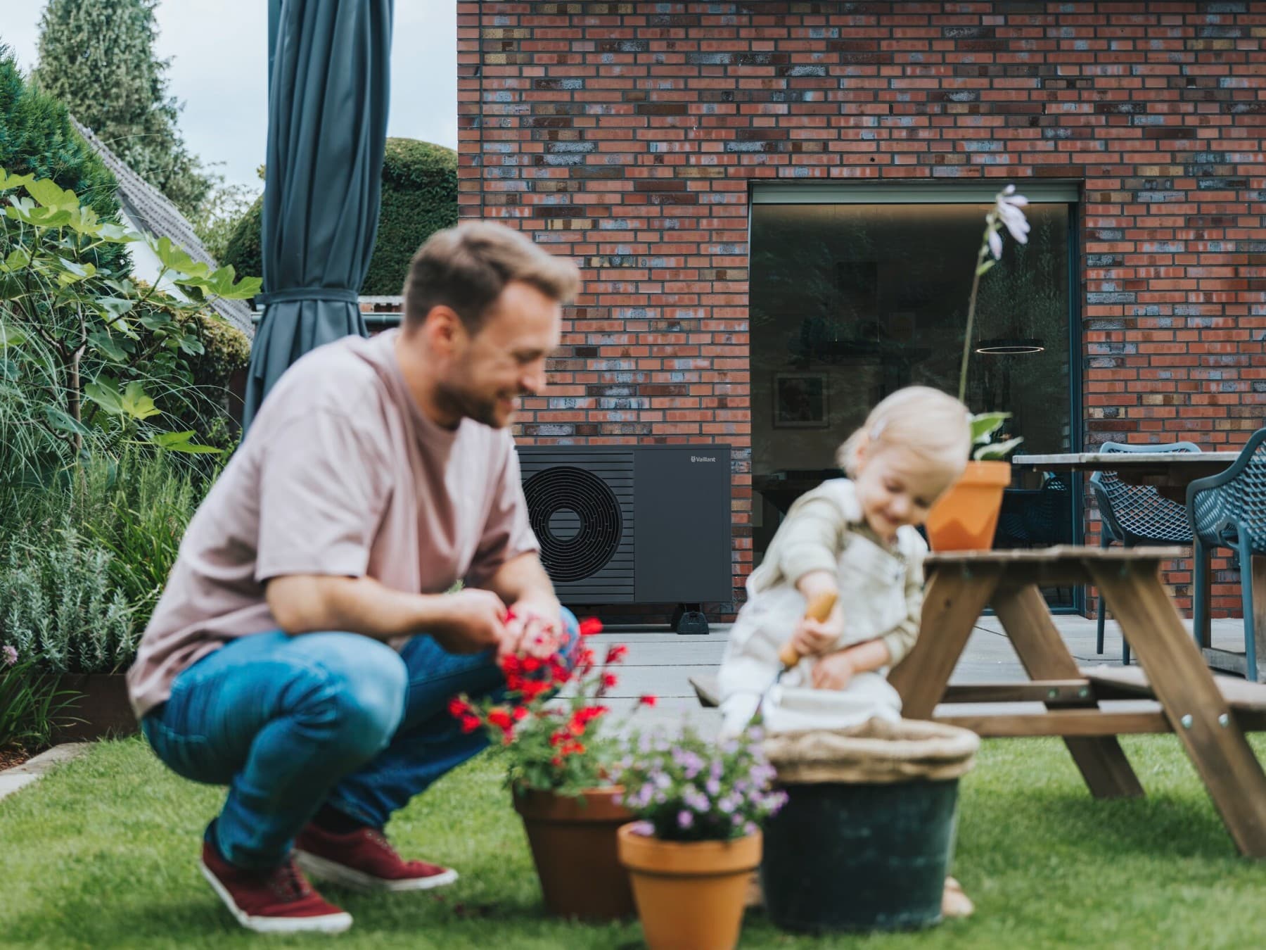 Man plant bloemen in de tuin, op de achtergrond zie je een zwarte warmtepomp tegen een rode bakstenen gevel