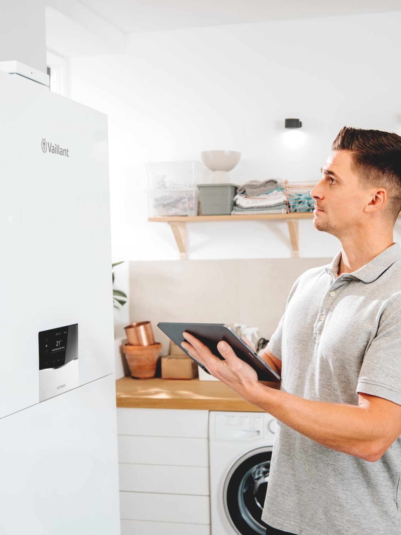 Installateur staat voor een geothermische warmtepomp van Vaillant met een tablet in zijn handen.