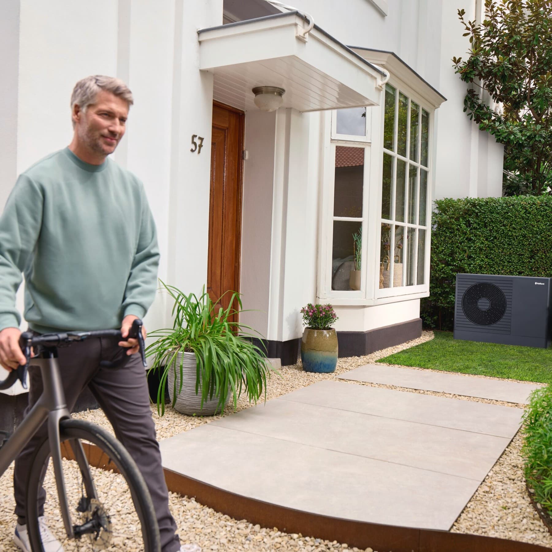 Man houdt zwarte fiets vast, op de achtergrond zie je een antracietkleurige warmtepomp van Vaillant