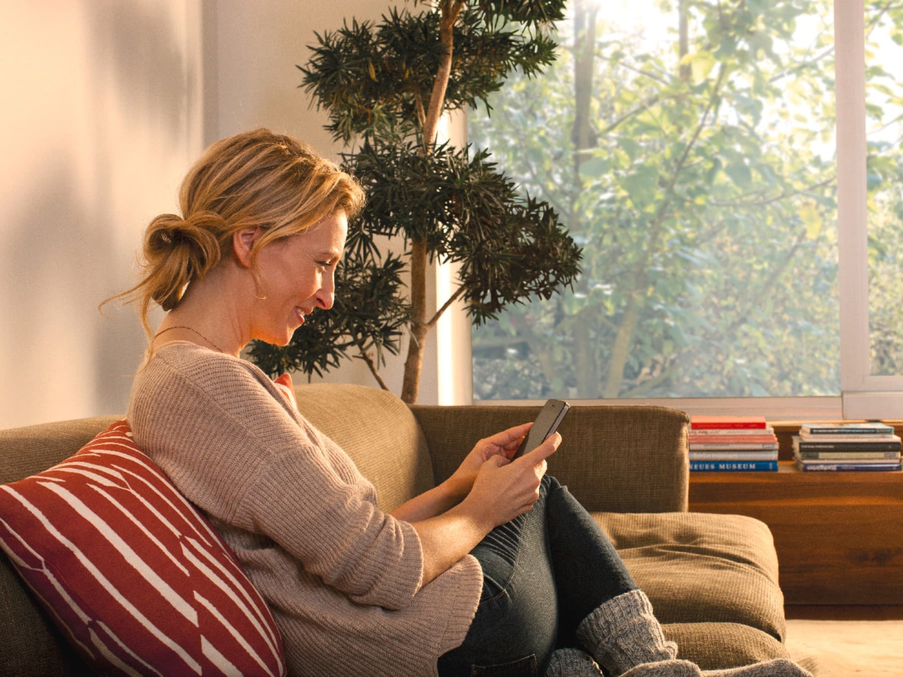 Vrouw zit op de bank en kijkt naar haar smartphone.