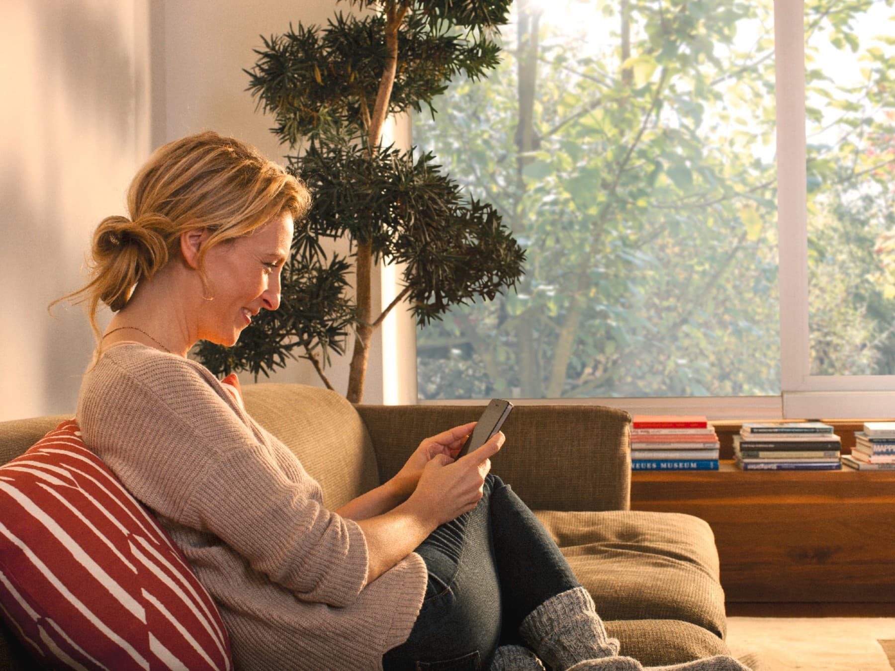 Une femme assise sur le canapé regarde son smartphone.