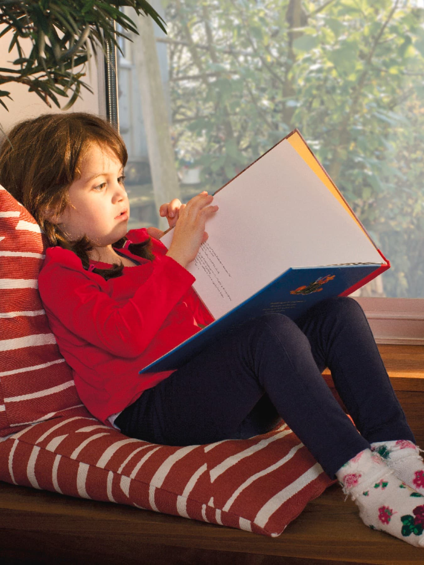 Un enfant lit un livre près de la fenêtre.