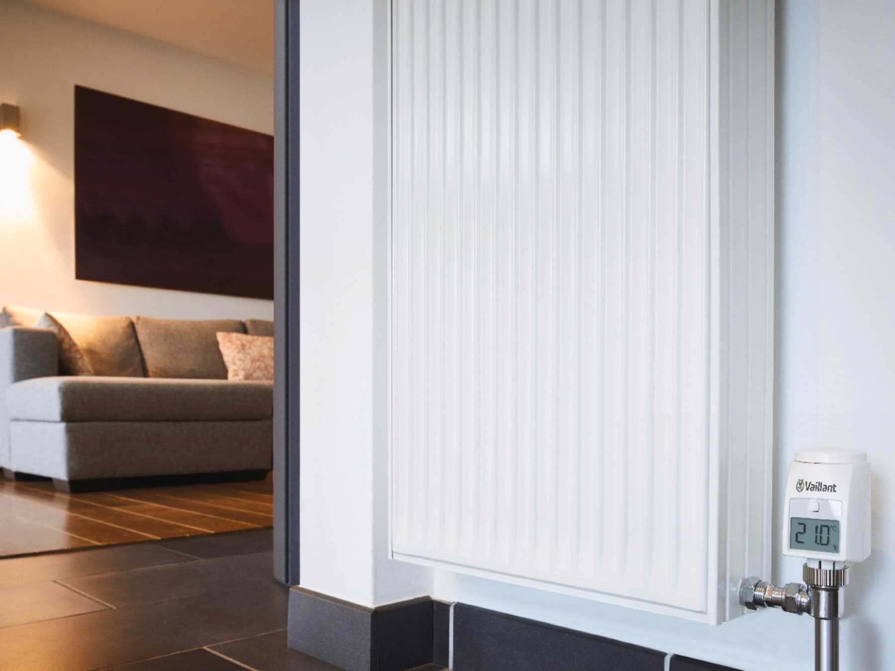 Een radiator met op de achtergrond een bank en sfeervolle verlichting; op het display van de radiator staat 21°.