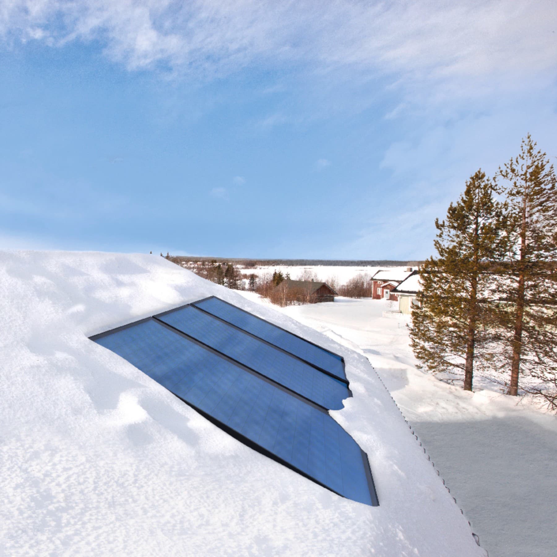 Ingebouwde zonnepanelen op een besneeuwd dak, op de achtergrond zie je blauwe lucht en een sneeuwlandschap met enkele huizen