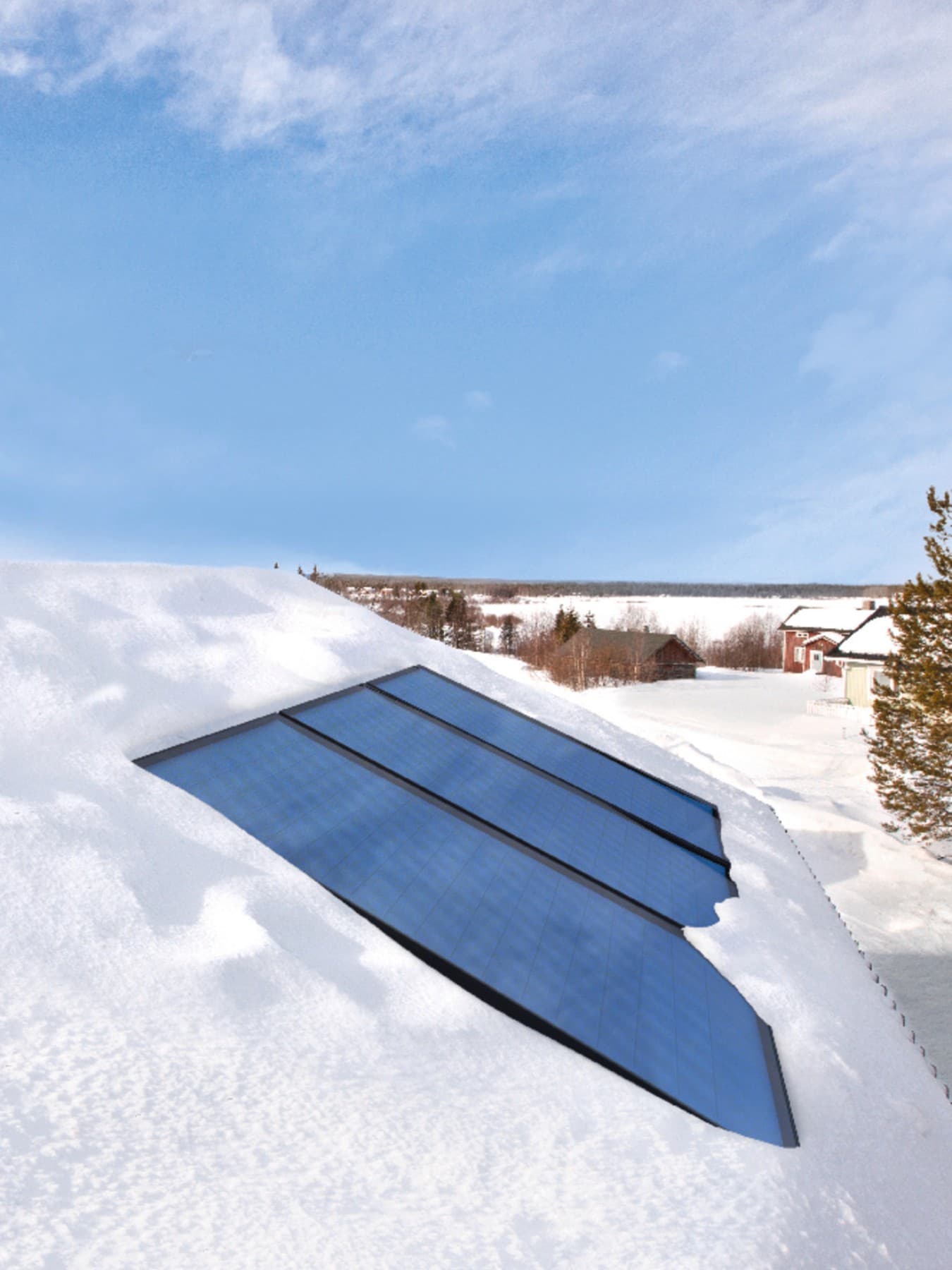 Ingebouwde zonnepanelen op een besneeuwd dak, op de achtergrond zie je blauwe lucht en een sneeuwlandschap met enkele huizen