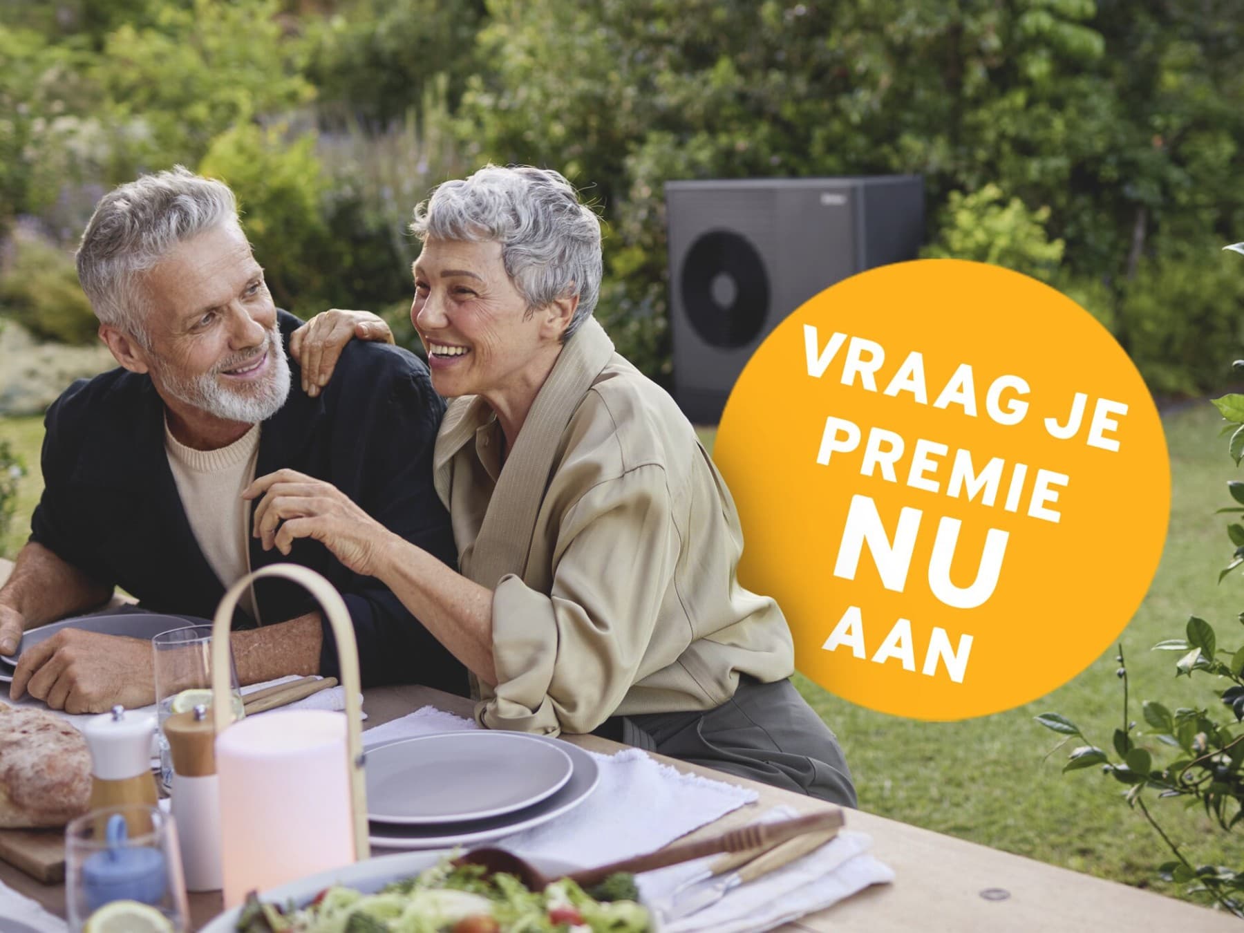 Koppel zit aan tafel in de tuin, op de achtergrond zie je een zwarte warmtepomp en op het beeld staat een gele bol met de tekst "Vraag je premie NU aan".