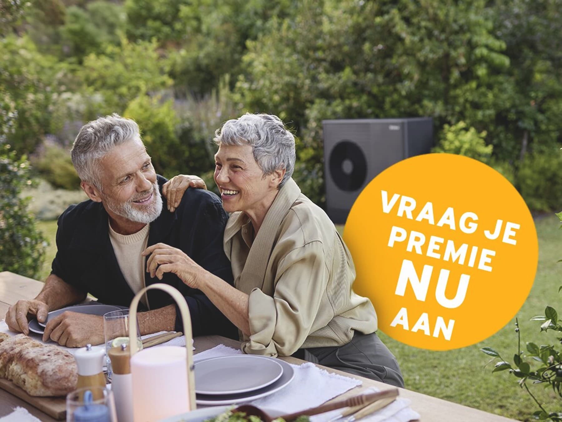 Een stel zit op het terras te eten; op de achtergrond is een warmtepomp te zien.