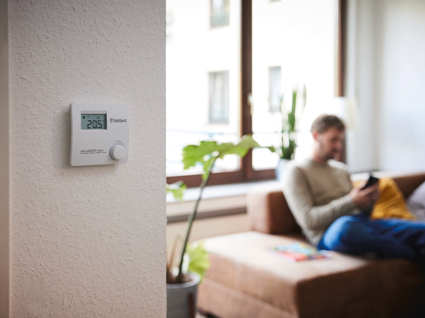 sensoROOM pure modulerende regeling tegen een muur, op de achtergrond een man die op zijn telefoon kijkt