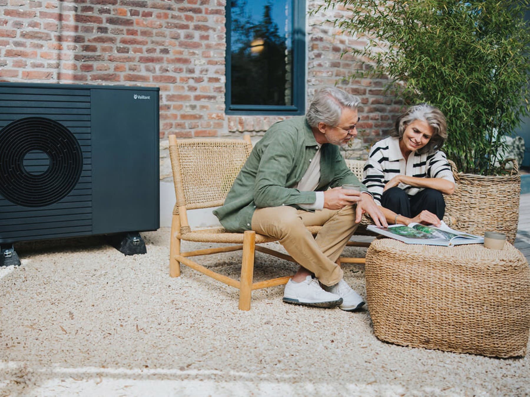 Een stel zit buiten in de tuin en bekijkt een brochure. Op de achtergrond staat een Vaillant-warmtepomp.