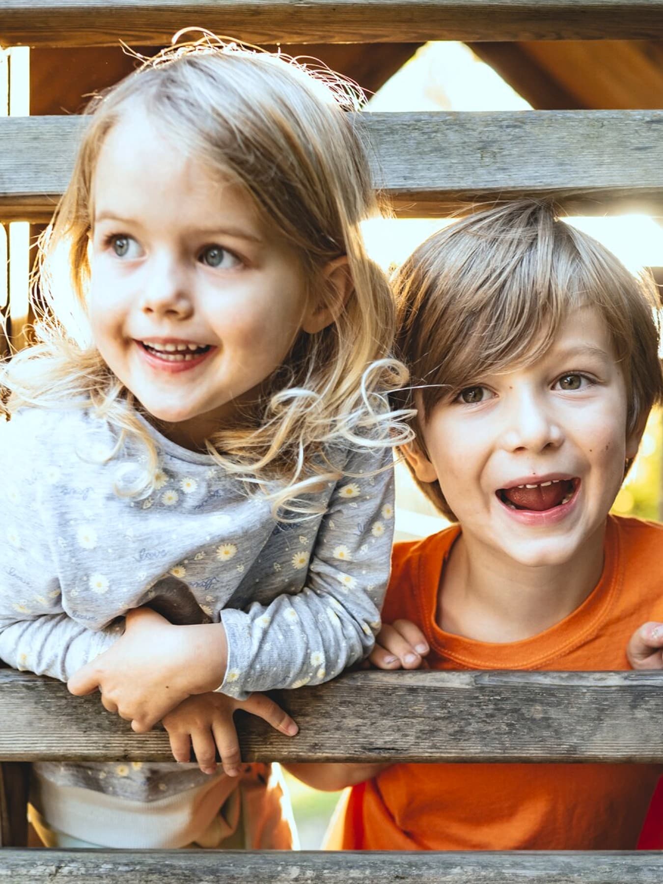 Twee kinderen spelen in een houten hut op een speelplaats.