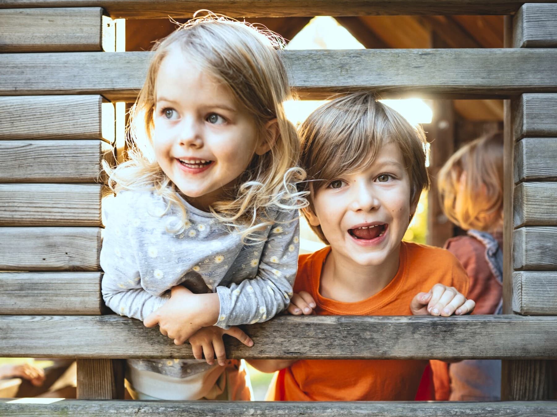 Twee kinderen spelen in een houten hut op een speelplaats.